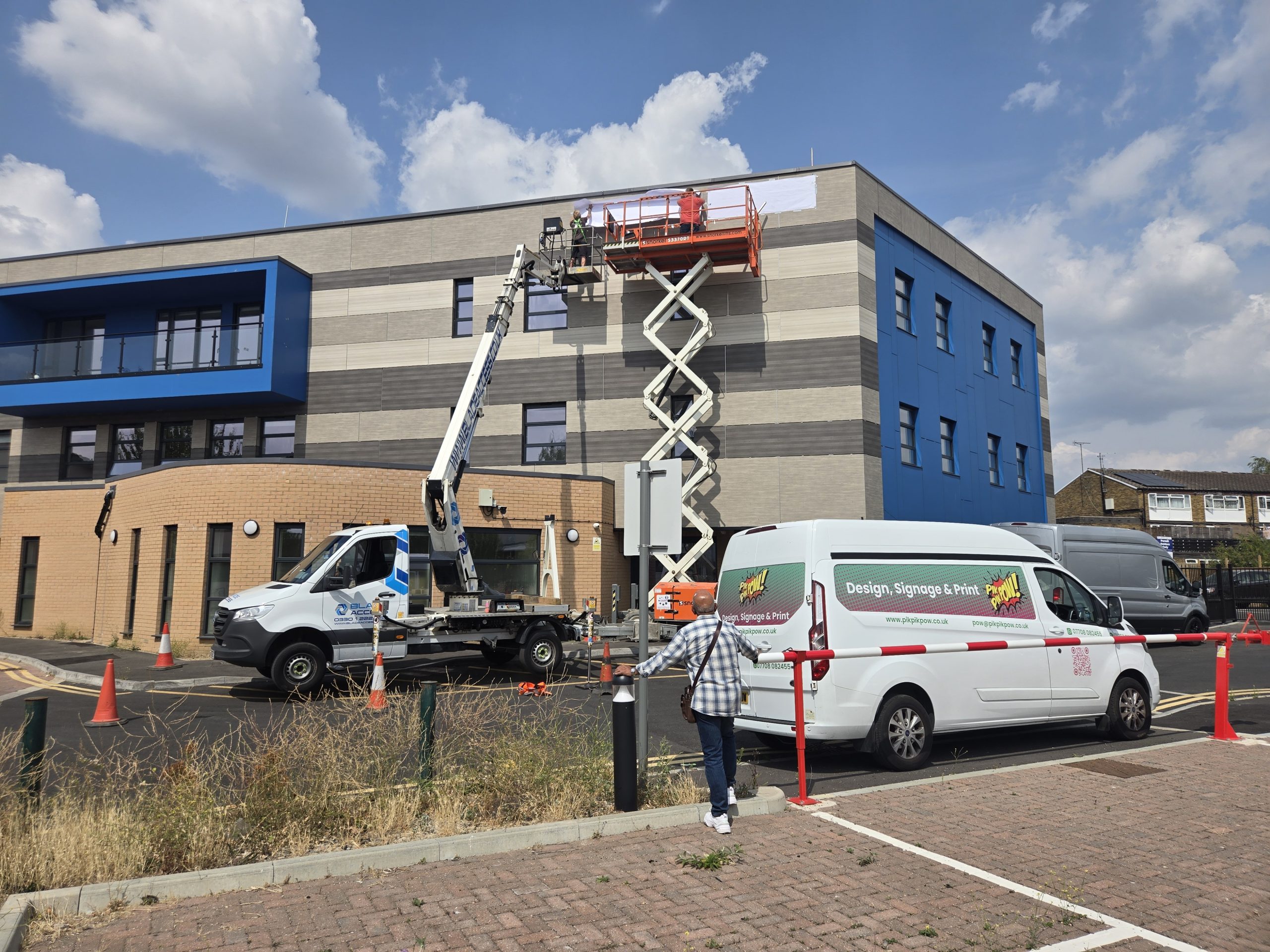 Sign installers using a scissor lift and truck-mounted platform at the Bharani building in Slough