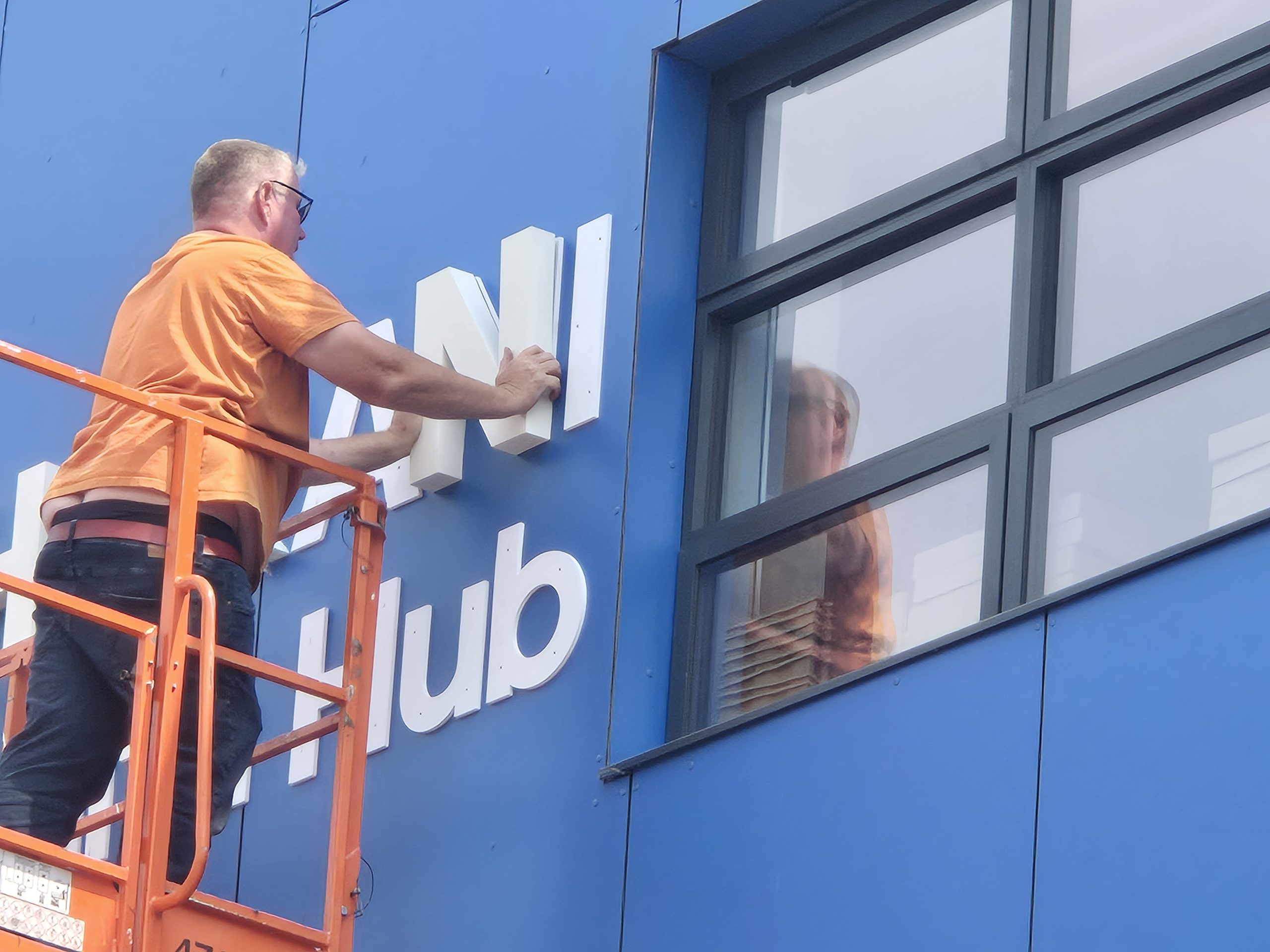Installer positioning white built-up lettering on the blue exterior of Bharani Health Hub