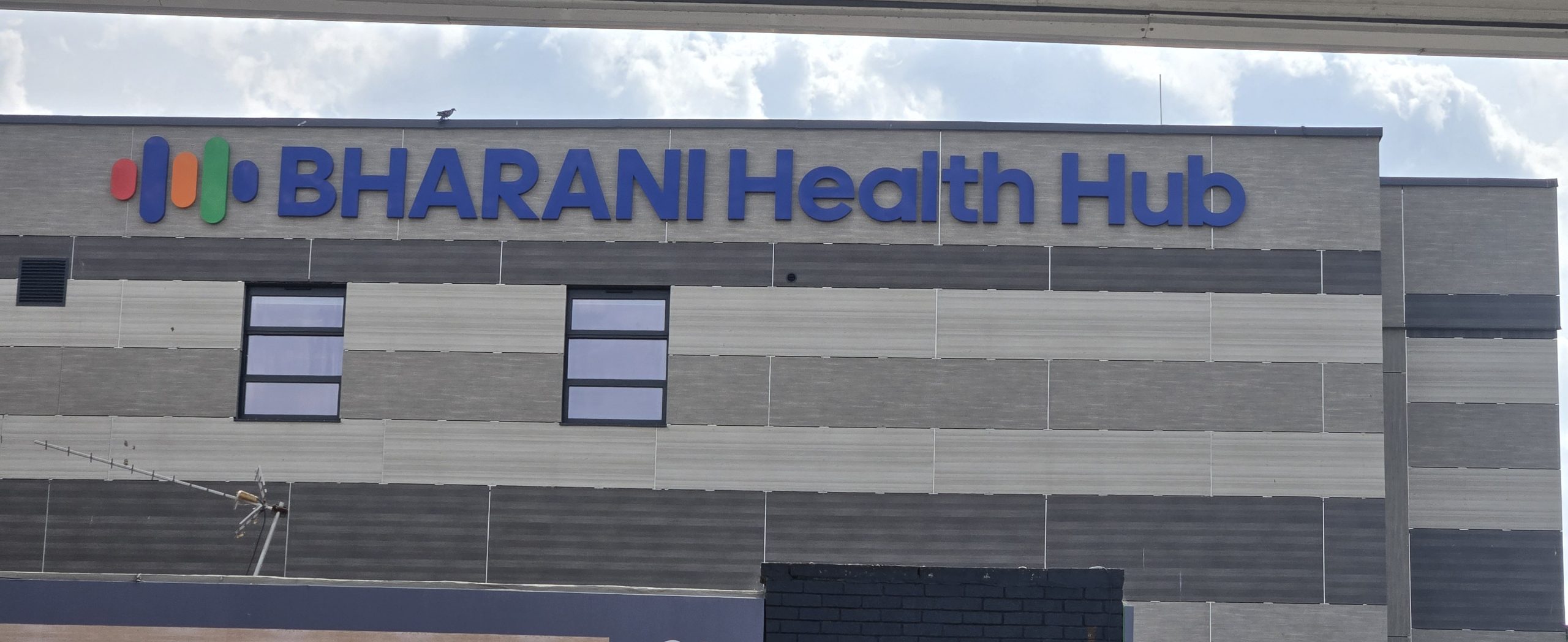 Completed blue Bharani Health Hub fascia lettering across the grey-clad building